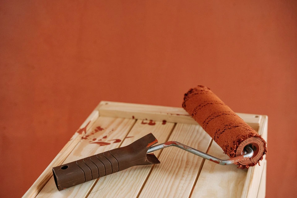 Rouleau de peinture orange posé sur une planche devant un mur orange
